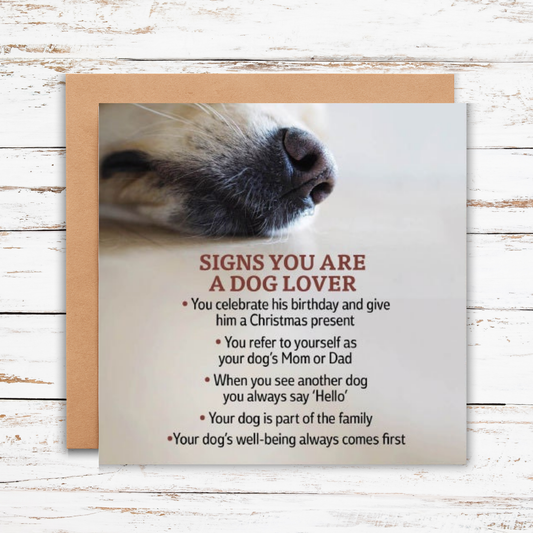 Card with dog's nose close-up and text about signs you are a dog lover on a wooden surface.