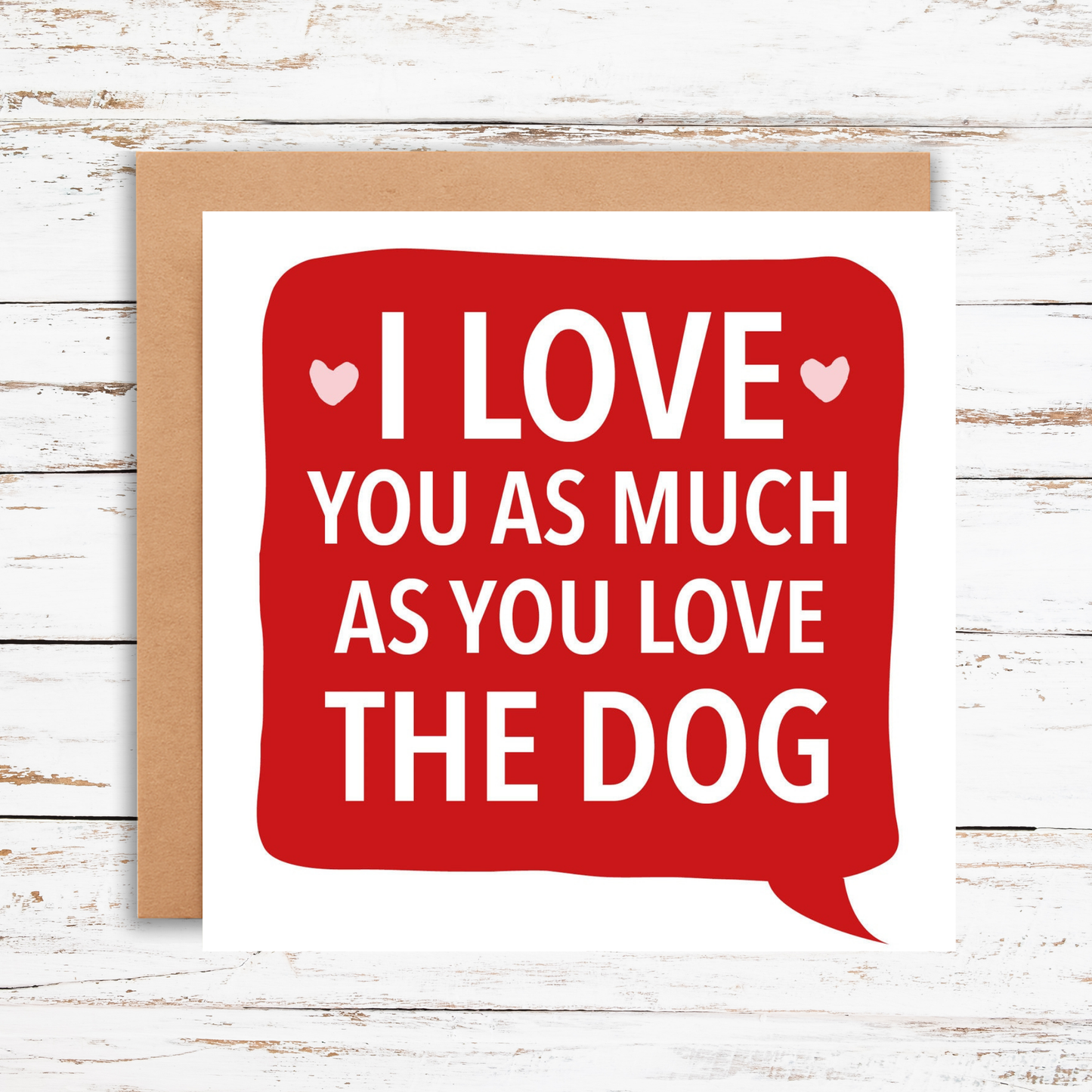 Card with red speech bubble saying 'I love you as much as you love the dog' on a wooden background