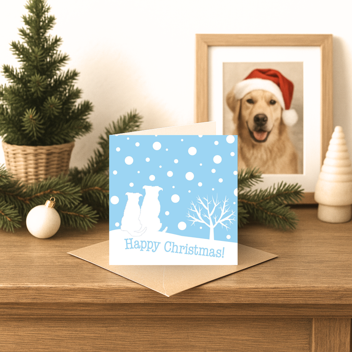 Christmas card with two dogs on a blue background, placed on a wooden surface with festive decorations.
