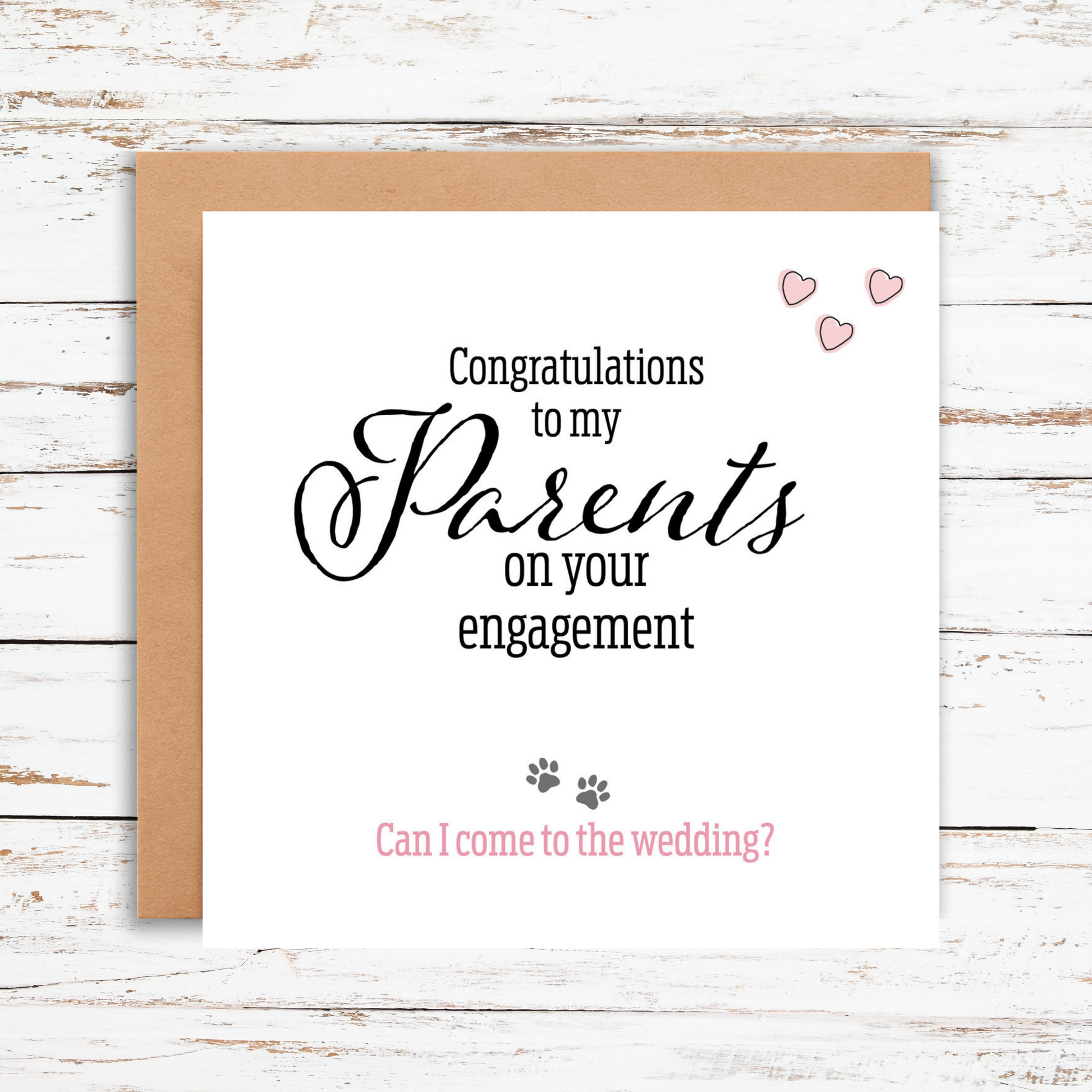 Greeting card with text 'Congratulations to my Parents on your engagement. Can I come to the wedding?' on a wooden surface.