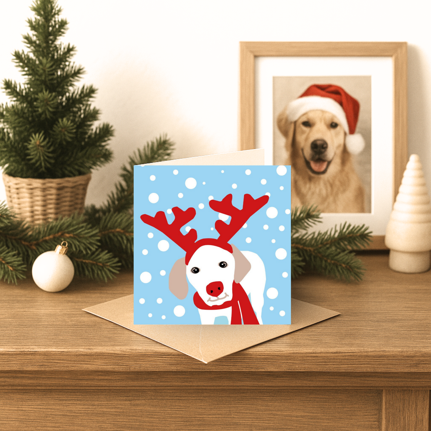 Christmas card with a dog wearing reindeer antlers on a wooden surface with festive decorations.