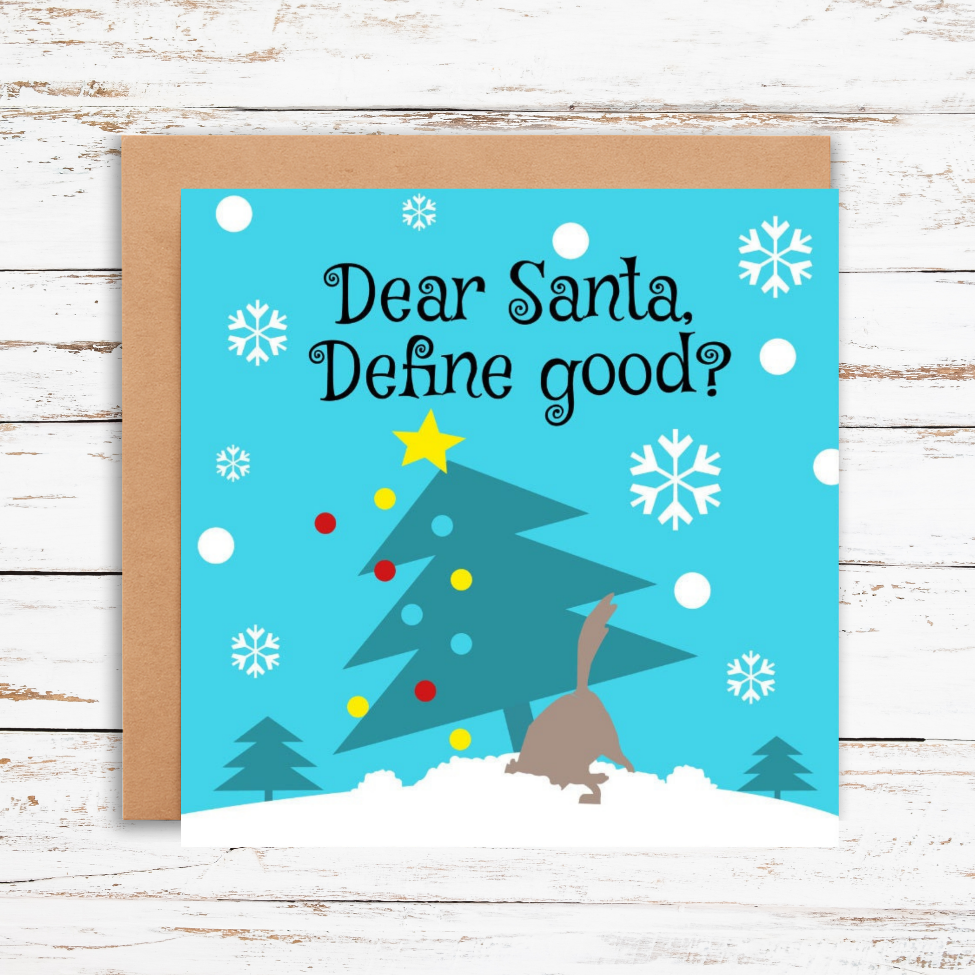 Christmas card with a tree and reindeer design on a blue background with snowflakes, on a wooden surface.