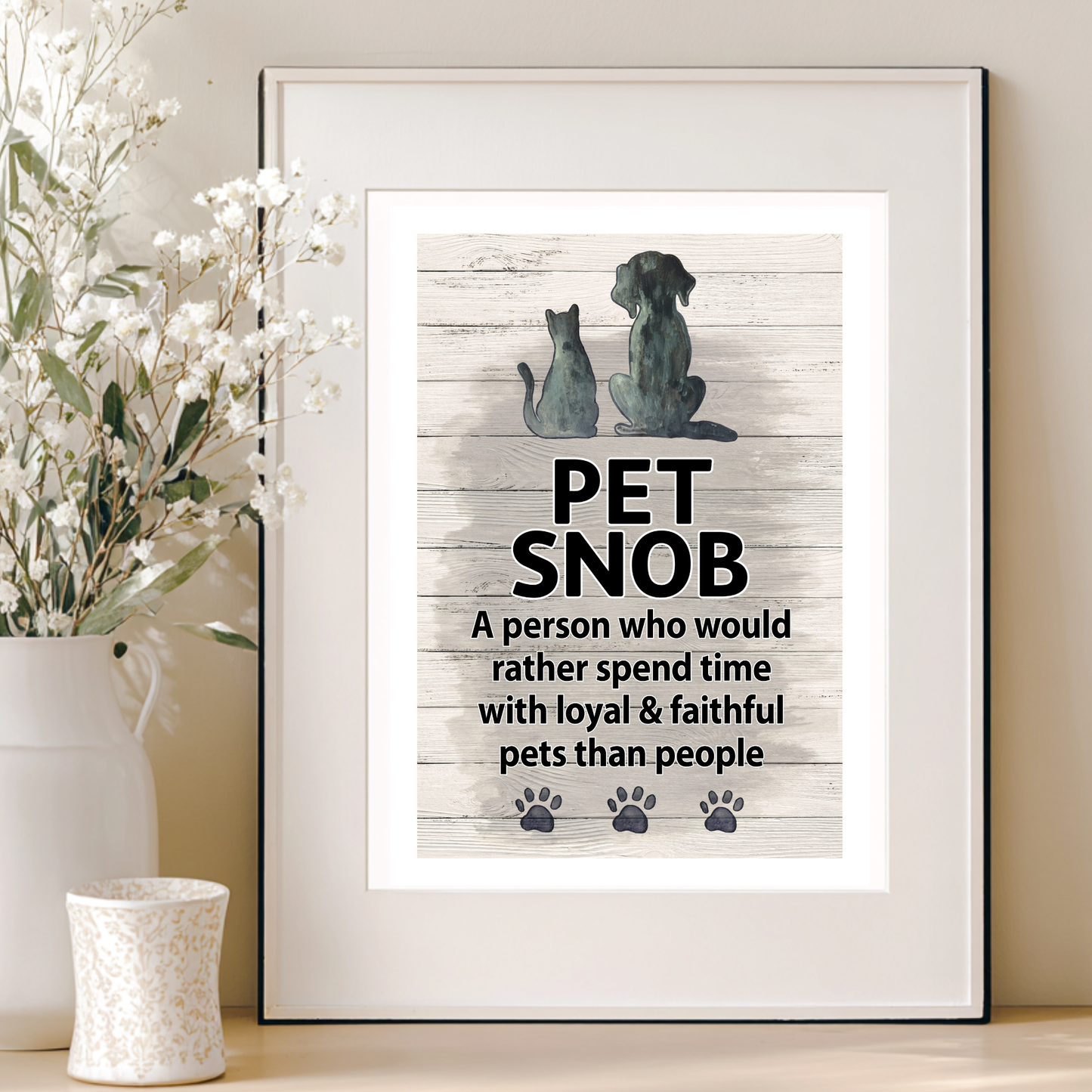 Framed artwork with dogs and text 'Pet Snob' on a wooden background, placed on a surface with decorative elements.